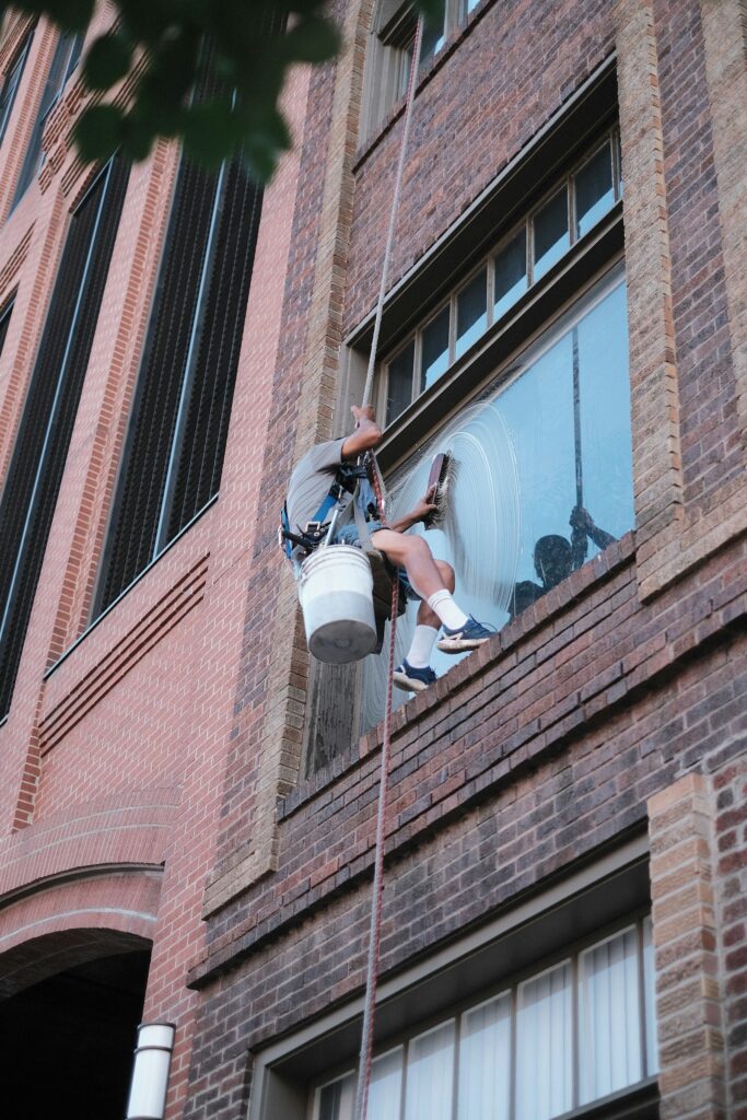 Glazenwasser op een ladder aan het werk bij een gebouw